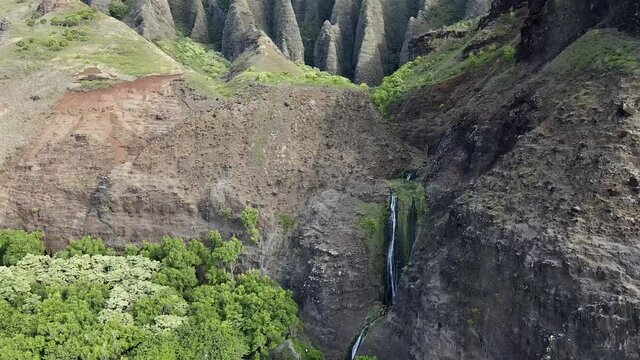 beautiful serene hawaii waterfall at kalalau beach in napali state park kauai hawaii midday dramatic mountain to beach landscape lush green tropical pan up with waterfall and steep cliffs