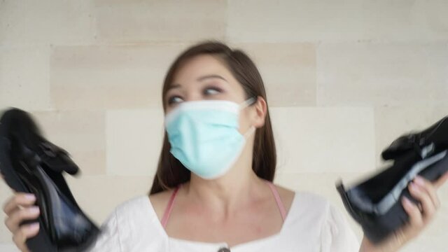 A young girl with big green eyes in a medical mask, rejoices in new beautiful black patent leather loafer shoes. 