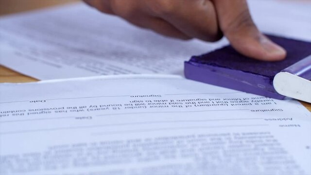 Male hand putting his thumb impression on legally approved bank papers / documents. Closeup shot of a young person's hand stamping with approved stamp / signing a contract papers