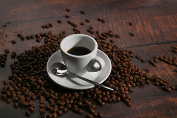 A cup of fragrant coffee and roasted coffee beans on wooden table.