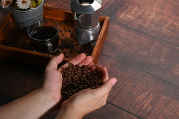 Man hands holding roasted coffee beans on wooden background.