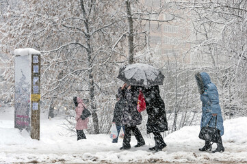 It is snowing heavily in the city. People hide from the snow under an umbrella