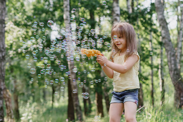 happy little girl blowing bubbles with a toy gun on a sunny summer day