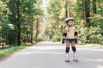 Little pretty girl on roller skates in helmet at a park. Cheerful preschool girl wearing inline roller skates and protective equipment