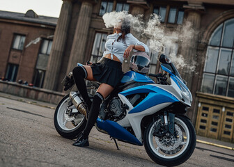 Obraz na płótnie Canvas Fashionable woman with sunglasses and vape posing on motorbike