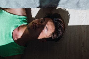 Portrait of pensive young handsome Chinese man lying on floor and looking away