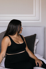 Naklejka na ściany i meble Pregnant Caribbean Indigenous woman sitting on bed relaxing