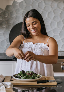 Young adult woman preparing salad for lunch in luxury kitchen