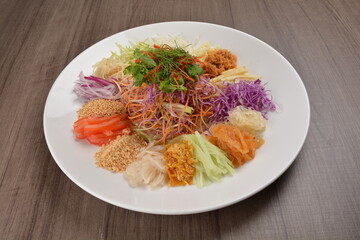 Chinese New Year festival colourful Yu Sheng Lo Hei salad with smoked salmon fish, cracker cookies and sweet sauce on wood background asian halal menu