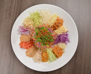 Chinese New Year festival colourful Yu Sheng Lo Hei salad with smoked salmon fish, cracker cookies and sweet sauce on wood background asian halal menu