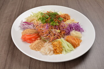 Chinese New Year festival colourful Yu Sheng Lo Hei salad with smoked salmon fish, cracker cookies and sweet sauce on wood background asian halal menu
