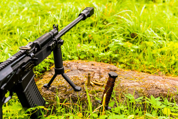 Rifle standing on a bipod with empty shells on the rock and combat knife stuck into the ground. Close up view of a stone level