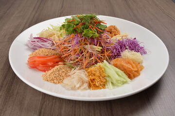 Chinese New Year festival colourful Yu Sheng Lo Hei salad with smoked salmon fish, cracker cookies and sweet sauce on wood background asian halal menu