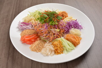 Chinese New Year festival colourful Yu Sheng Lo Hei salad with smoked salmon fish, cracker cookies and sweet sauce on wood background asian halal menu