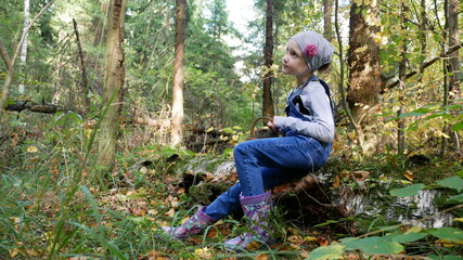 A girl sits on a tree in the woods and dreams. The girl collects mushrooms. The girl dreams in the...