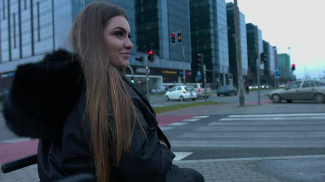 A handicapped woman sitting in a wheelchair waiting on the zebra cross side. A woman with a disability expressing a positive attitude while waiting for the traffic lights to give her right to cross.