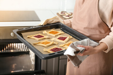 Woman holding baking tray with uncooked Danish pastry in kitchen