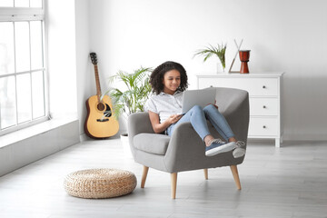 African-American girl with laptop sitting in armchair at home