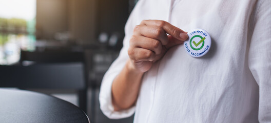 Closeup image of a woman putting Covid-19 vaccinated sign brooch on shirt