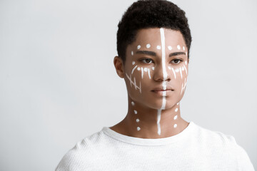 Young African-American guy with paint on face against light background