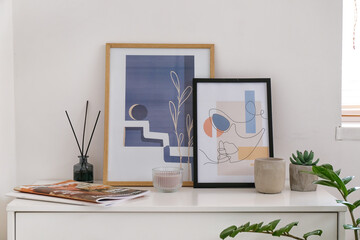 Stylish pictures and reed diffuser on shelf near light wall