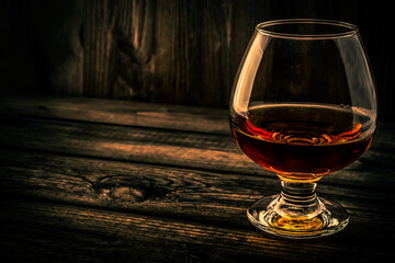Glass of brandy and on an old wooden table. Angle view