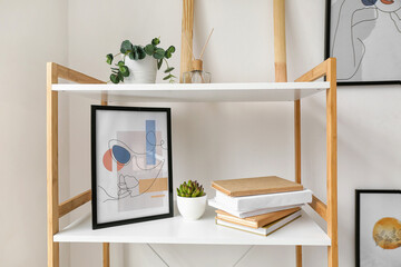 Book shelf with picture and houseplants near light wall