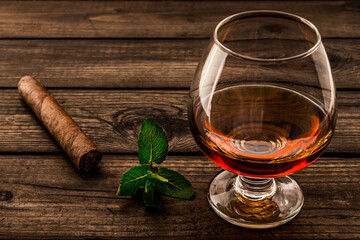 Glass of brandy with mint sprig and cuban cigar on an old wooden table. Close up view