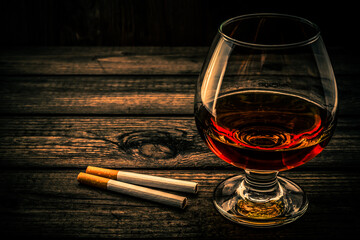 Glass of brandy with two cigarettes on a old wooden table. Angle view