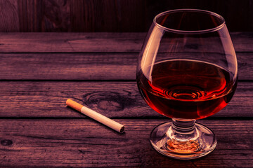 Glass of brandy and cigarette on a old wooden table. Angle view