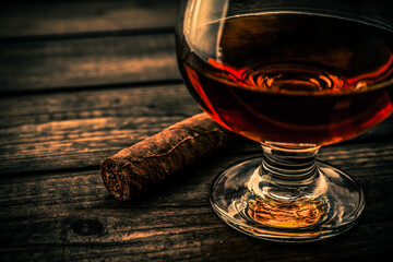 Glass of brandy and cuban cigar on an old wooden table. Close up view, shallow depth of field