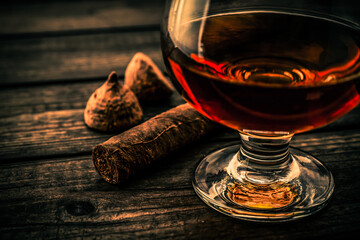 Glass of brandy and a couple of chocolate truffles with cuban cigar on an old wooden table. Close up view, shallow depth of field