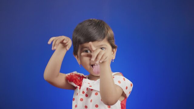 Litte girl kid with tongue out or grimacing dancing by hands up on blue background - happy, cheerful and crazy kids concept