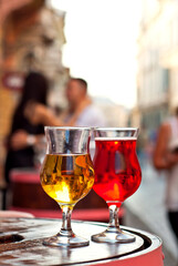 Glass of red and white wine close up. Alcoholic liqueur on a wooden barrel on a background of the city. Blurred couple kissing in the background.