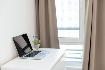 Cropped shot of modern workspace with blank screen laptop on white table with white wall background