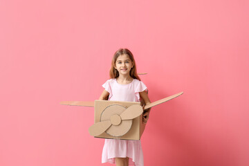 Little girl with cardboard airplane on color background