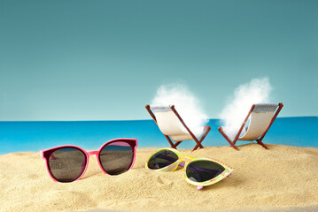 Pink glasses on the sand close up. Glasses on a beach chair background. Beach chairs on a background of blue water and sky. White cloud sunbathes on the beach.