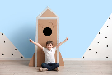 Cute little boy playing with cardboard rocket near color wall
