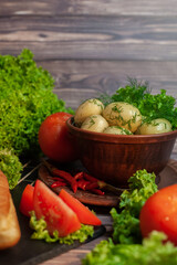 Boiled potatoes with dill in a brown ceramic bowl, stands on the dining table. Lettuce leaves, tomato and red pepper. Snack for lunch