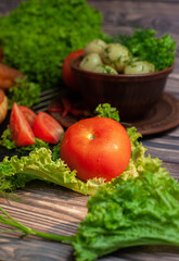 A large red tomato lies on the table on the table on a leaf of green lettuce, with boiled potatoes