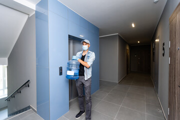 Courier in face mask with clipboard and bottles of cooler water in entryway. Delivery during coronavirus quarantine