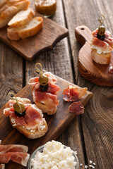Tasty bruschettas with cheese, prosciutto and olives on wooden background