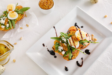Tasty bruschetta with eggs and arugula on light background