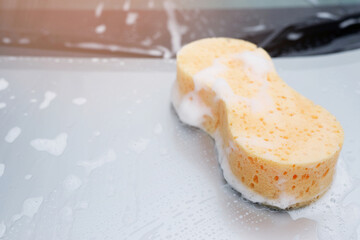Yellow sponge and soap over the car for washing. Motor hood being cleaned. Concept car wash clean. Leave space for writing messages.