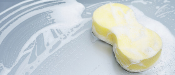 Yellow sponge and soap over the car for washing. Motor hood being cleaned. Concept car wash clean. Leave space for writing messages.