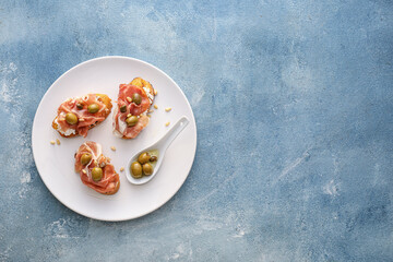 Tasty bruschettas with cheese, prosciutto and olives on color background
