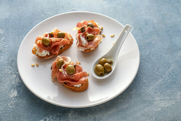 Tasty bruschettas with cheese, prosciutto and olives on color background