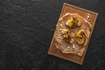 Tasty bruschettas with cheese and grilled zucchini on dark background