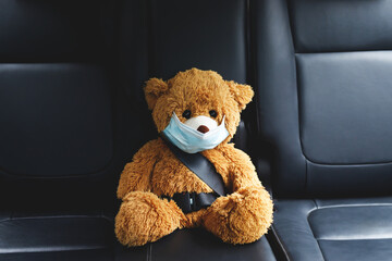 A brown teddy bear wearing a mask sits in the car.