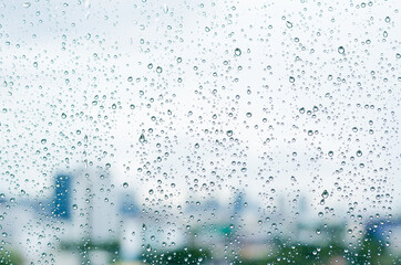 Rain drop on glass window at day time in monsoon season with blurred city buildings background.